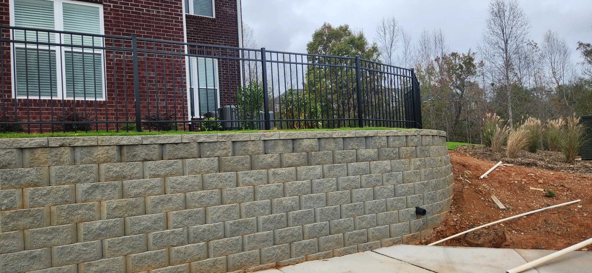 Black aluminum fence atop curved segmental retaining wall red brick house belmon