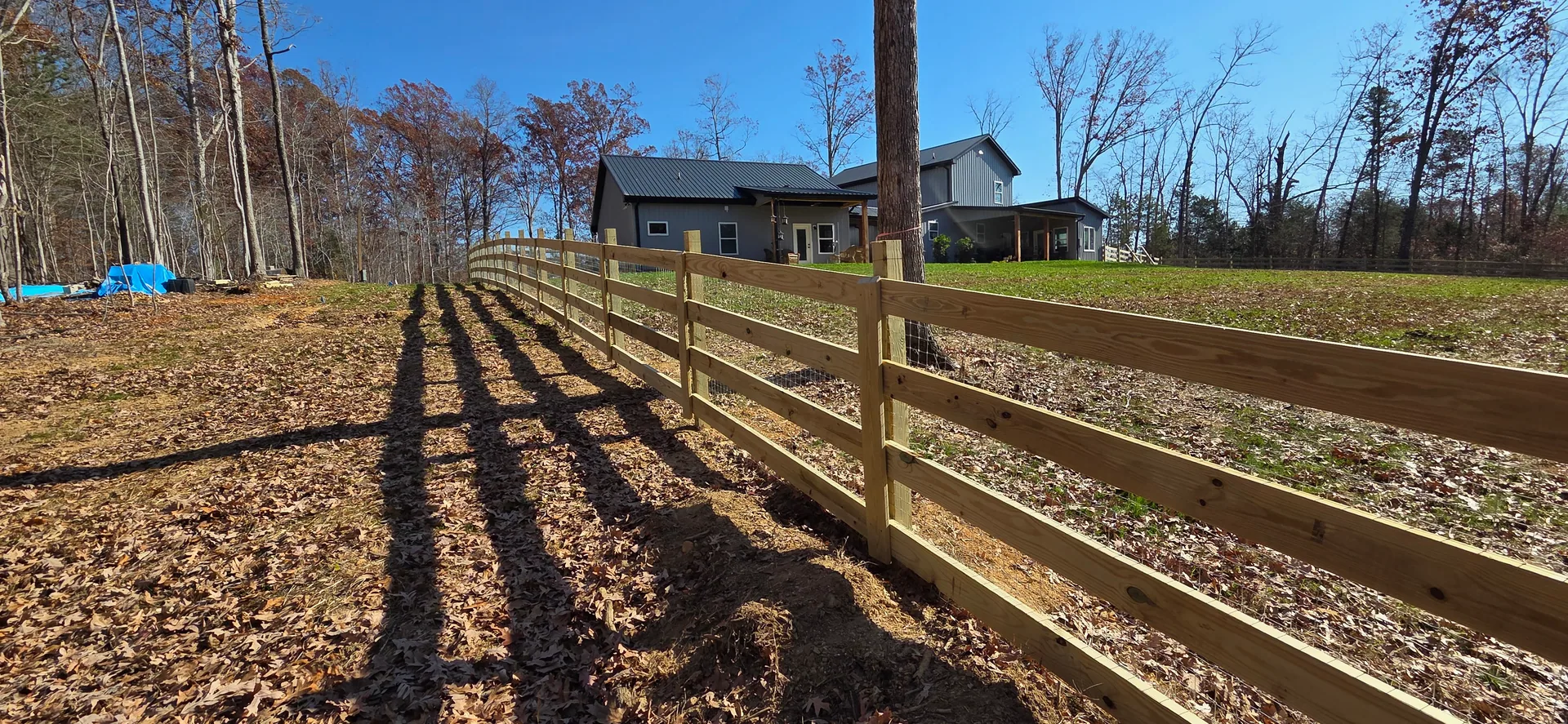 Long four board wood pasture fence leaf covered ground gray metal roof home crow