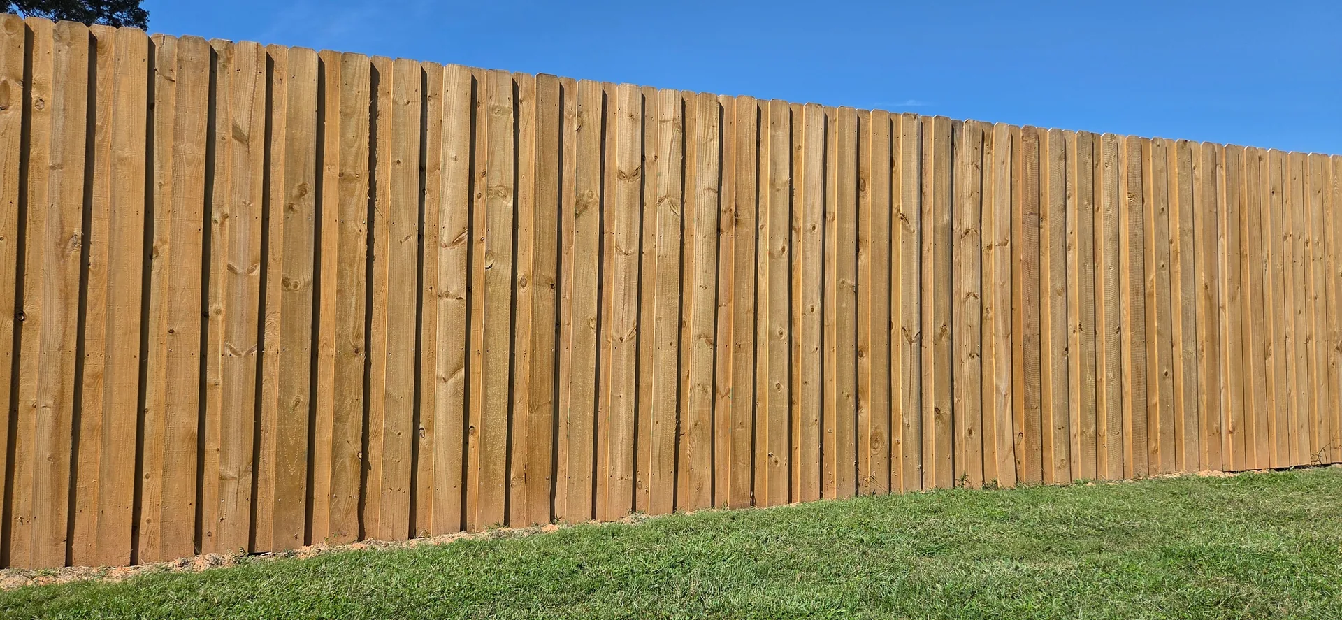 Low angle board on board wood fence grass slope blue sky dallas nc