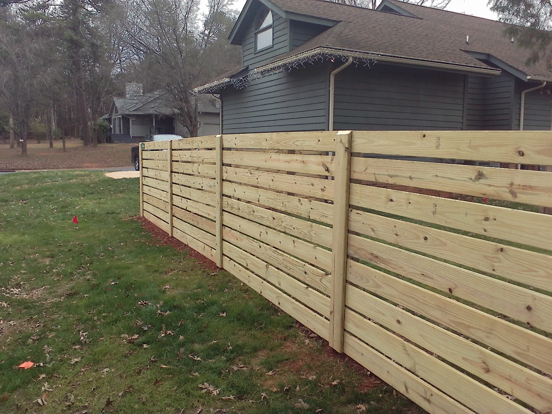 New horizontal slat wood fence gray house corner lawn survey flags gastonia