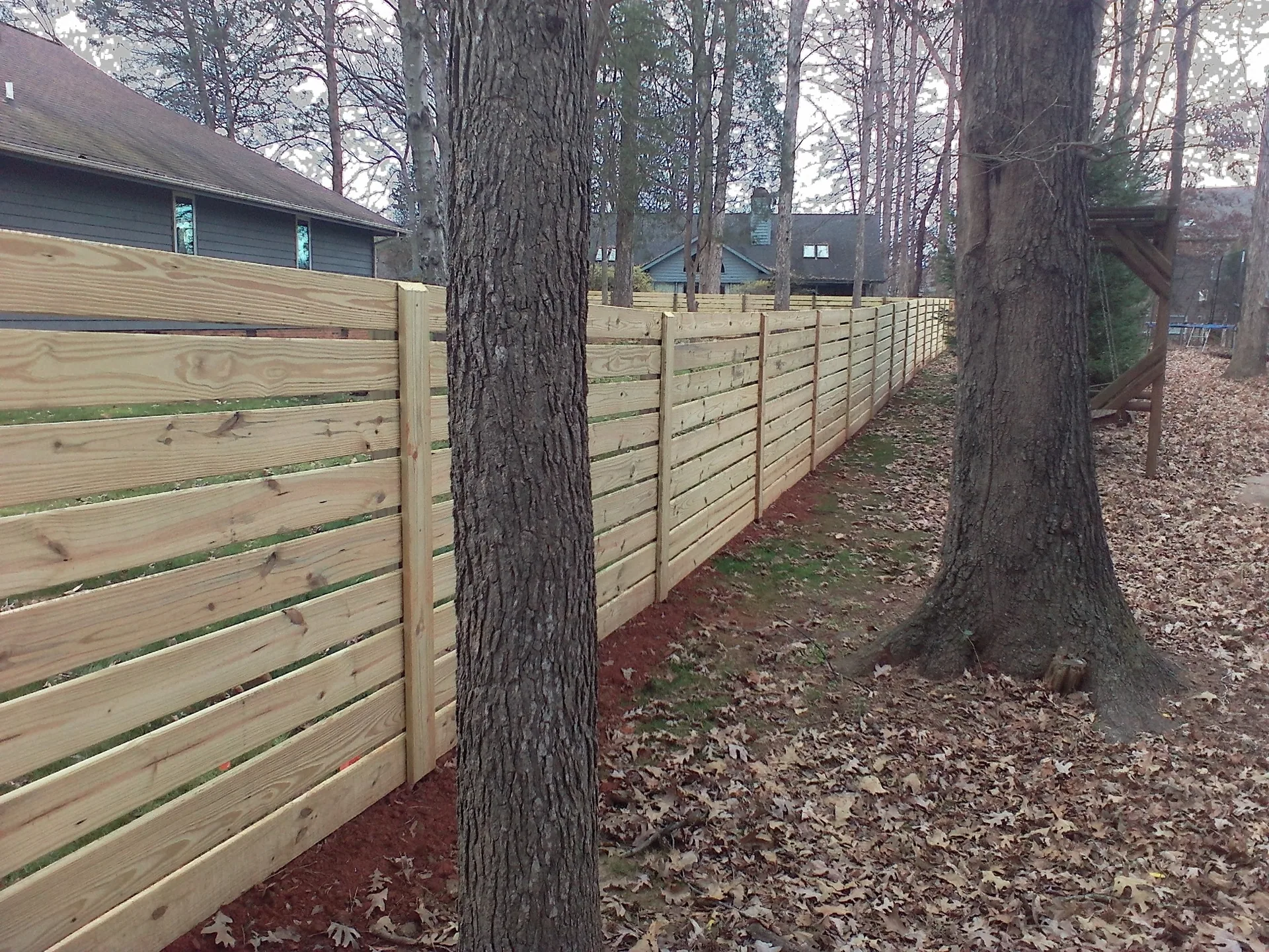 Spaced horizontal board wood fence oak trees leaf covered backyard belmont nc
