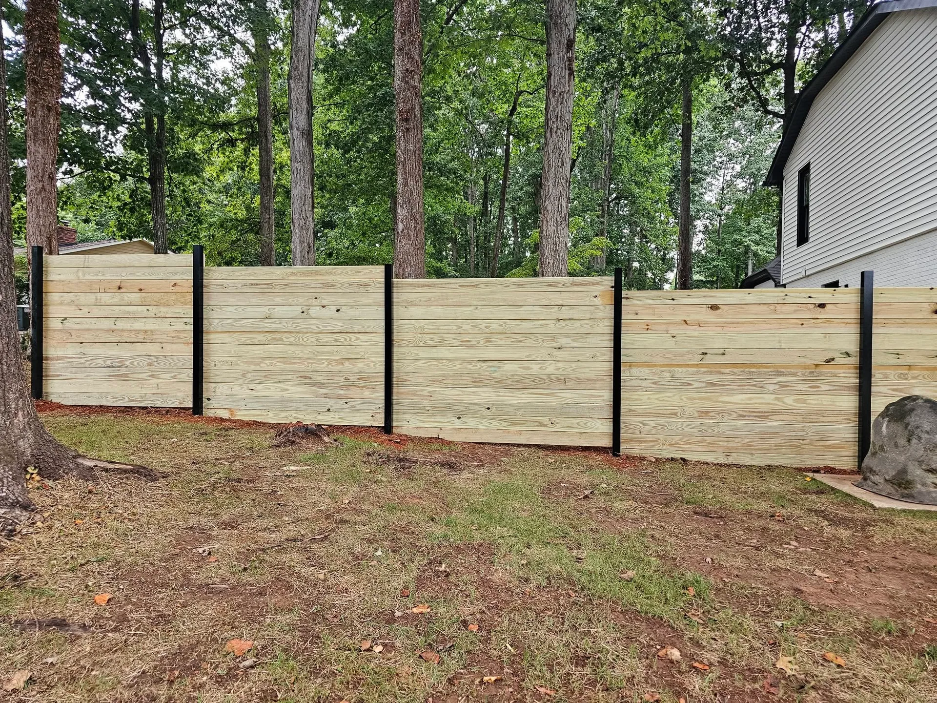 Stepped horizontal pine board fence black posts large boulder backyard gastonia