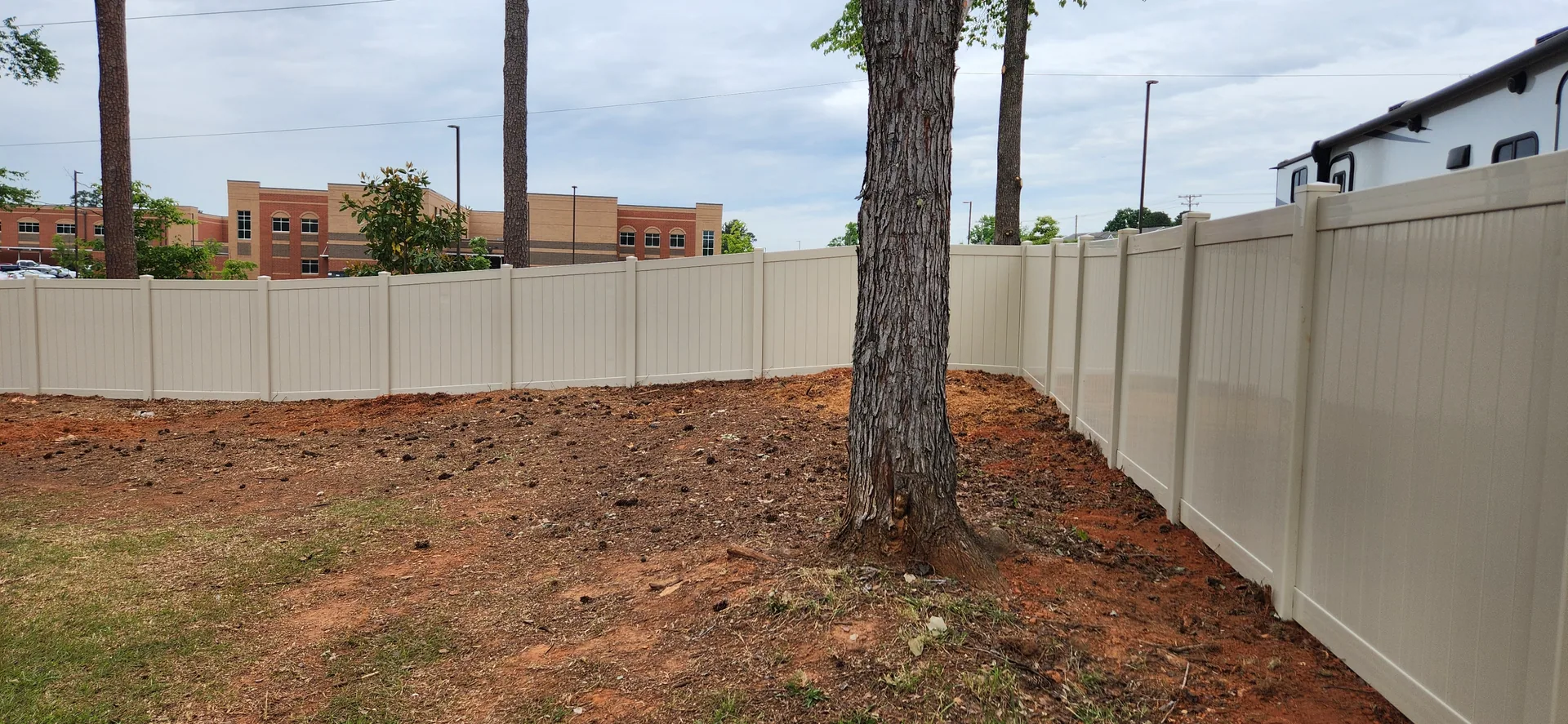 Tan vinyl privacy fence corner pine tree bare red clay yard bessemer city