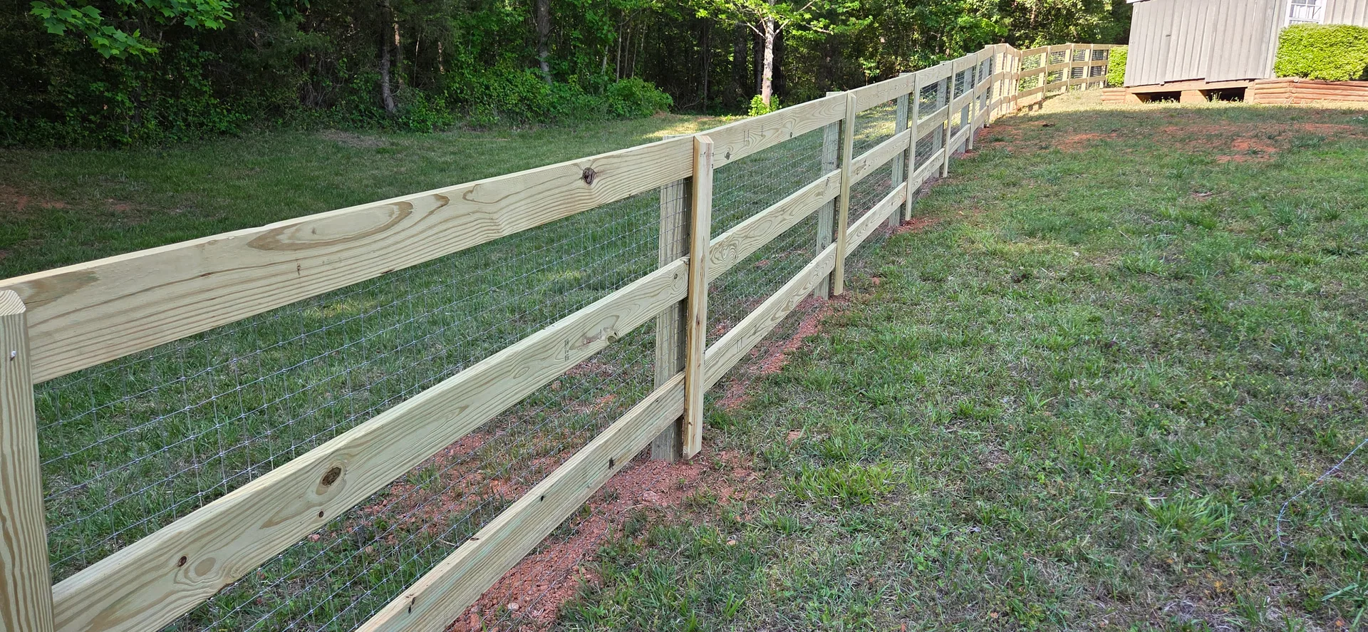 Three board wood fence welded wire sloped grass treeline dallas nc