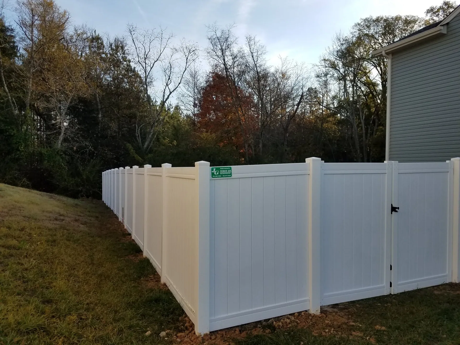 White vinyl privacy fence walk gate corner sloped yard treeline gastonia nc